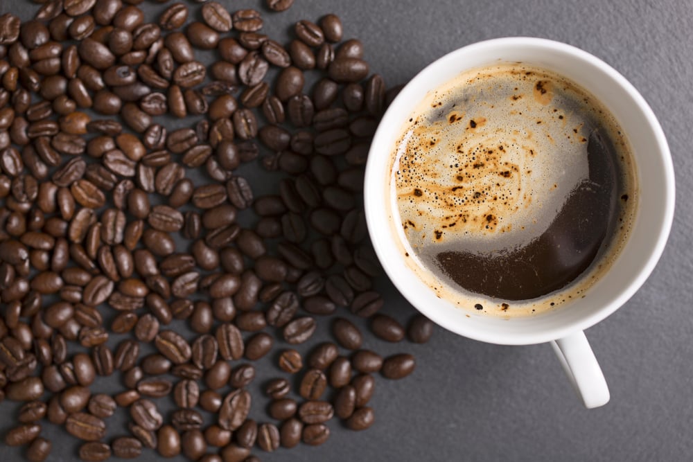 Still life of fresh roasted coffee beans with a white mug on a black slate surface